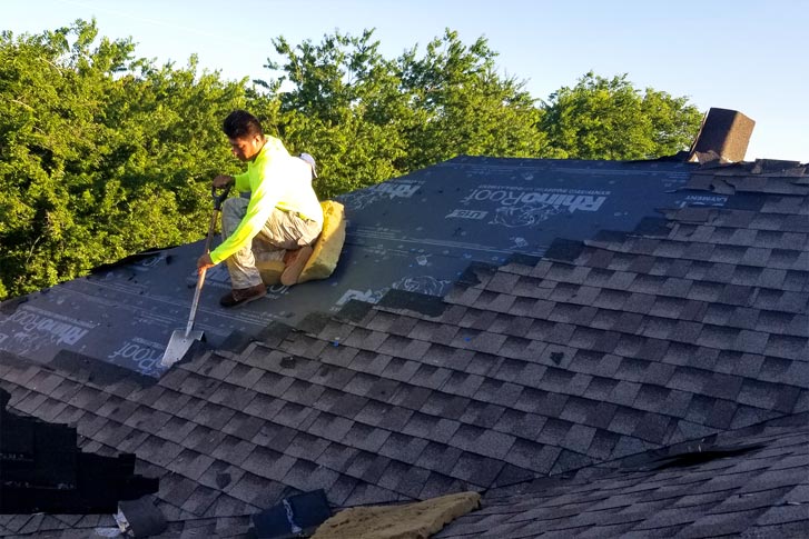 Worker removing shingles from a roof in McKinney TX